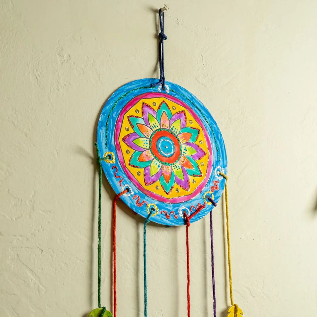 NESTA TOYS - Colorful mandala design on a circular wall hanging with strings against a beige wall.